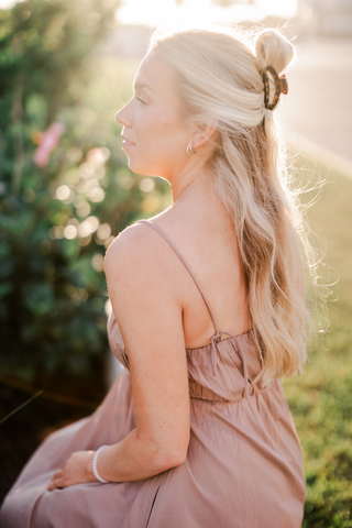 Woman wearing tortoise hair clip in blonde hair, shown in profile with soft natural lighting outdoors.