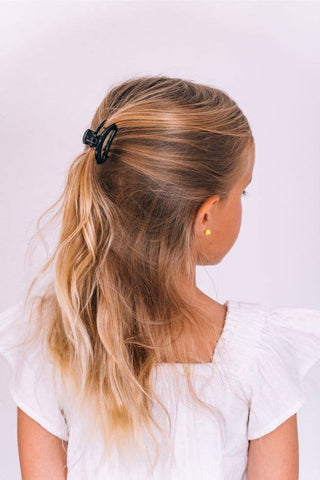 Woman wearing black small open hair clip in blonde ponytail against white background