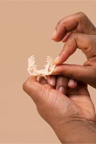 Hands gently holding a small decorative hair clip with an intricate open design against neutral background.