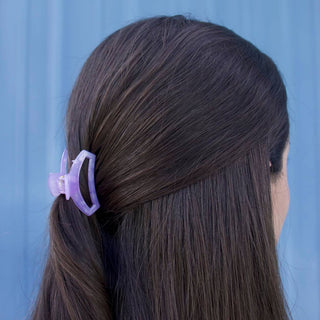 Woman with dark hair wearing a small purple open hair clip against blue background