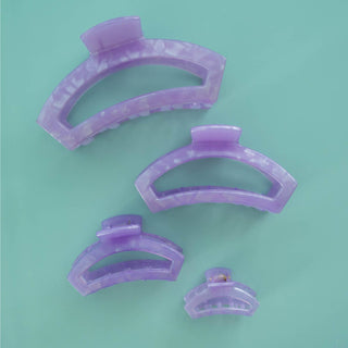 Four purple translucent hair clips in different sizes arranged on a mint green background.