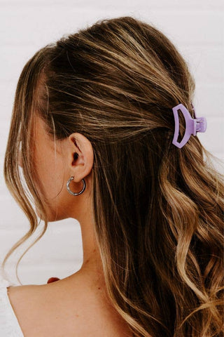 Woman with wavy brown hair wearing a small lilac open hair clip and silver hoop earrings.