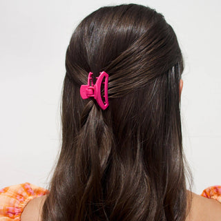 Woman wearing bright pink open hair clip in dark brown hair, showing back view styling