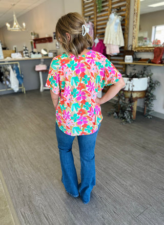 Woman wearing colorful floral v-neck top with jeans, shown from behind in boutique setting.