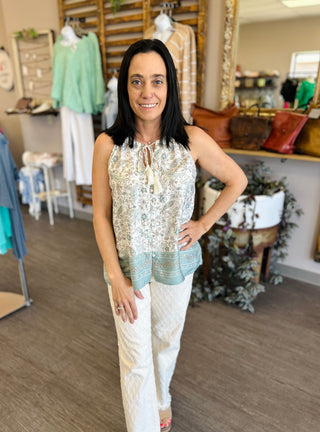 Woman wearing paisley print sleeveless top with tie neckline and white pants in clothing boutique