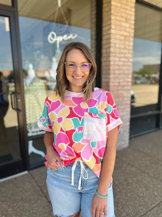 Woman wearing Haptics Paradise Floral Top with chest pocket and drawstring hem, paired with denim shorts.