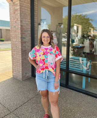 Woman wearing Haptics Paradise Floral Top paired with denim shorts, standing outside boutique storefront.