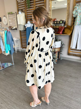 Woman wearing white polka dot dress with black spots in clothing boutique store