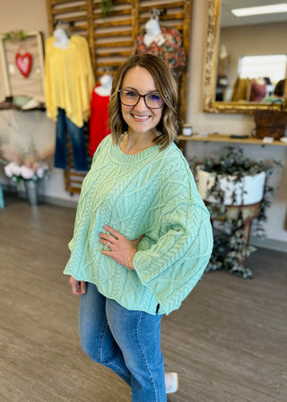 Woman wearing mint green cable knit sweater in boutique clothing store setting