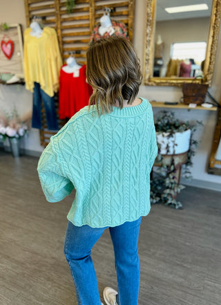 Woman wearing mint green cable knit sweater and jeans in clothing boutique store setting