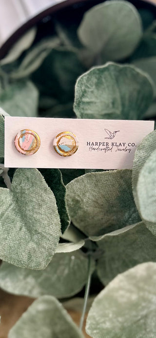 Harper Klay Co. Pastel Mirage Stud Earrings displayed on white card against green leafy plant background.