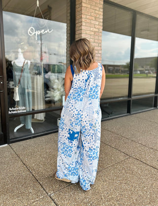 Woman wearing Haptics Patchwork Petals Wide Leg Overalls, back view, outside boutique storefront.