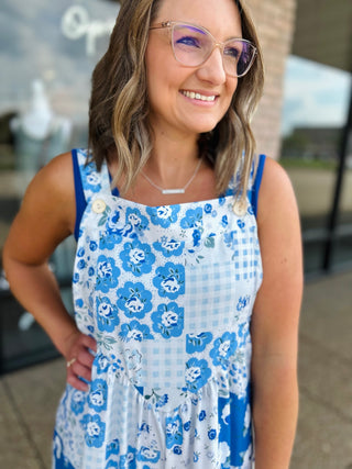 Smiling woman wearing blue floral patchwork wide leg overalls with gingham accents and button details.