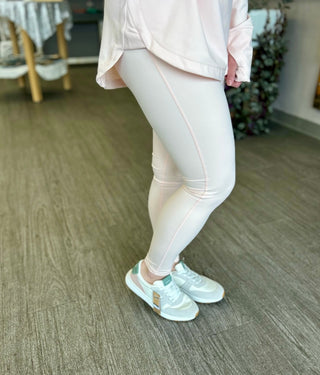 Woman wearing light pink tummy control leggings with matching top and mint sneakers on wooden floor