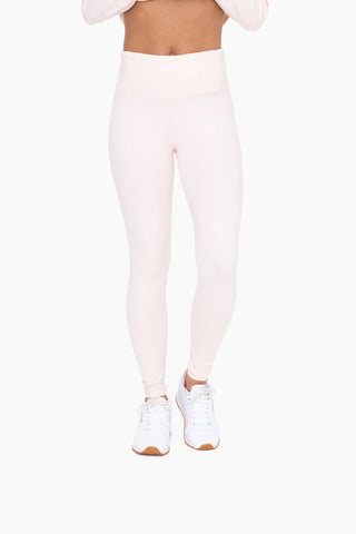 Woman wearing light pink high-waisted tummy control leggings with white sneakers on white background