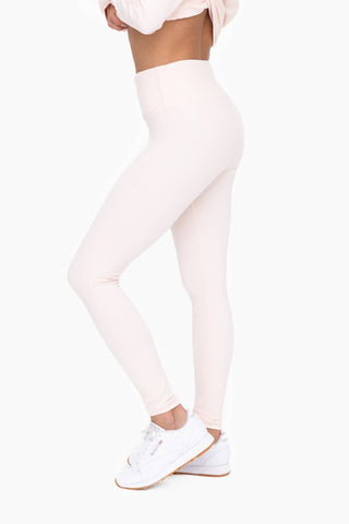 Woman wearing pink high-waisted tummy control leggings with matching crop top and white sneakers