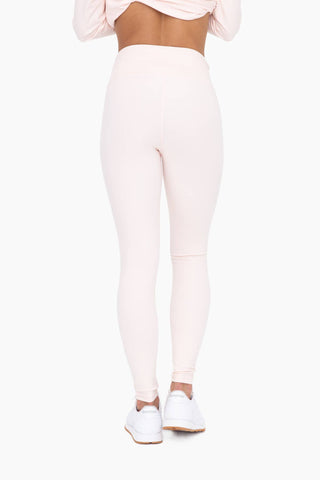 Woman wearing high-waisted pink leggings and matching crop top with white sneakers against neutral background
