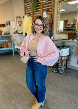 Woman wearing pink oversized cardigan over tan top with jeans in boutique setting