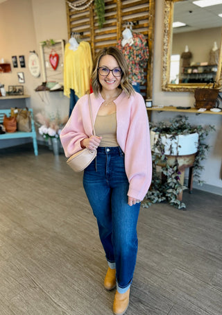 Woman wearing pink cardigan over tan top with jeans in boutique store setting