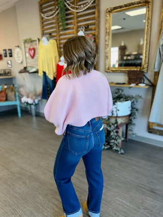 Woman wearing pink knit cardigan and blue jeans standing in boutique store setting