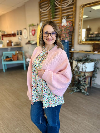 Woman wearing pink ribbed knit cardigan over floral top and jeans in boutique setting