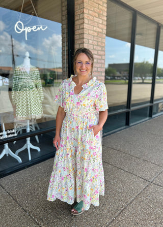 Woman wearing colorful floral midi dress with short sleeves standing outside boutique storefront.