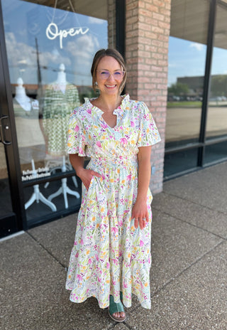 Woman wearing floral midi dress with short sleeves and smocked waist standing outside storefront