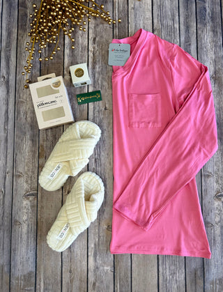 Pink long sleeve sleep shirt with pocket displayed on wooden surface with slippers and accessories