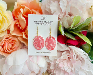 Pink scalloped oval earrings on Harper Klay Co card displayed among soft pastel flowers