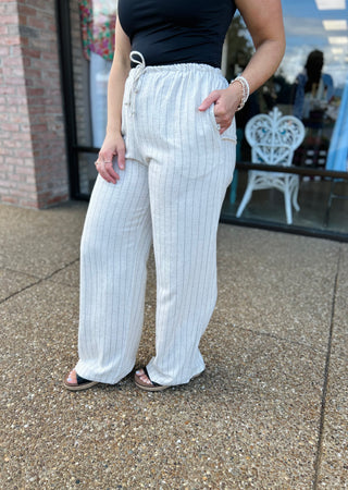 Woman wearing white pinstripe linen pants with drawstring waist and pockets, paired with navy top.