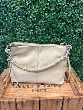Pistachio chain detail satchel crossbody bag displayed on wooden crate against green foliage background