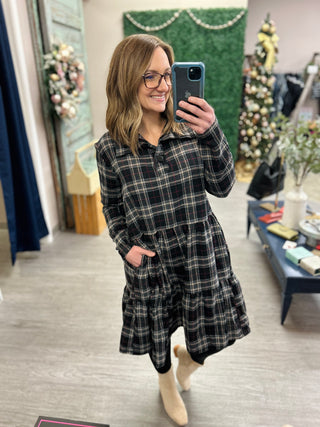 Woman wearing plaid button-up dress with tiered skirt taking mirror selfie in boutique store