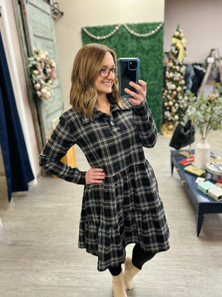 Woman wearing plaid shirt dress taking mirror selfie in boutique store