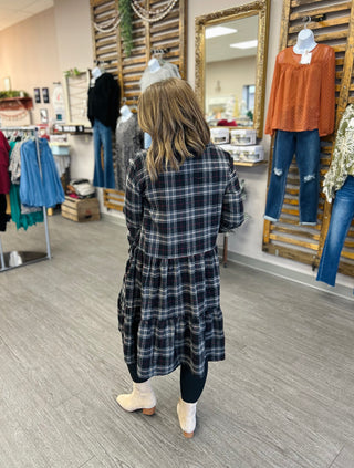 Woman wearing plaid tiered dress walking through clothing boutique, shown from behind