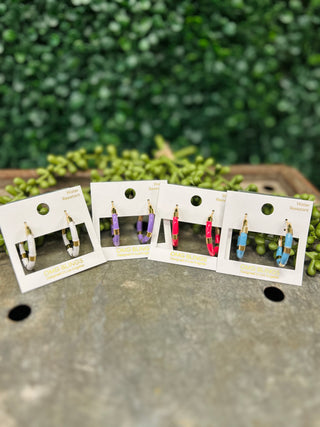 OMG Bling Playful Pop Hoops earrings displayed on white cards against green foliage background