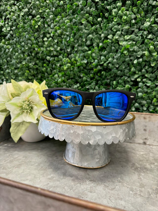 Stayson polarized sunglasses with blue lenses displayed on decorative stand with flower and greenery background