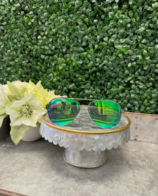 Polarized sunglasses with green-tinted lenses displayed on decorative glass stand with flower and foliage background.