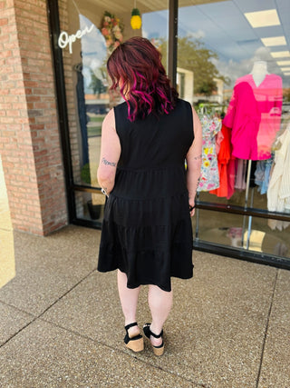 Woman wearing black tiered sleeveless dress standing outside clothing boutique storefront