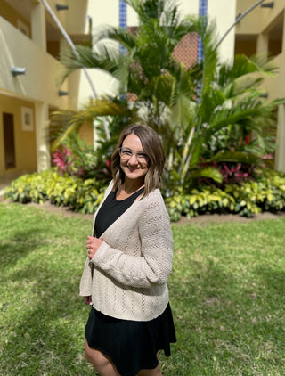 Woman wearing black athletic dress with beige cardigan standing on grass in tropical courtyard setting