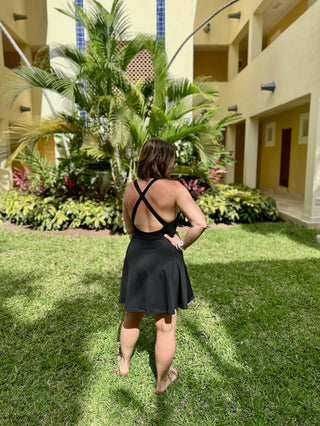 Woman wearing black athletic dress with crossed back straps standing on grass at resort.