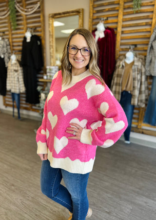 Woman wearing pink heart-patterned sweater with cream trim and blue jeans in clothing boutique