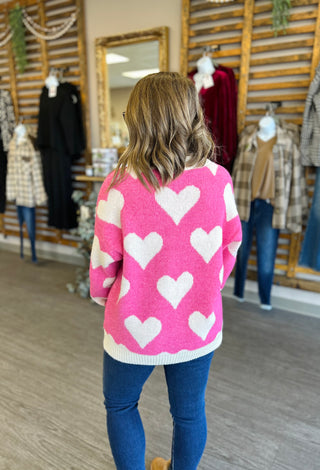 Woman wearing pink sweater with white heart pattern viewed from behind in clothing boutique