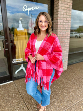 Woman wearing a cozy plaid fringe wrap poncho, paired with jeans, standing outside a boutique.