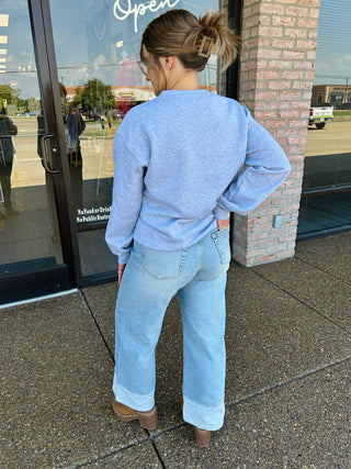 Woman wearing an embroidered sweatshirt with wide-leg jeans, shown from behind outside a boutique.