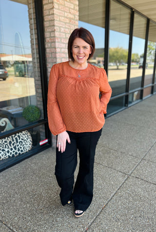 Woman wearing orange polka dot long-sleeve blouse with black pants, standing outside storefront.