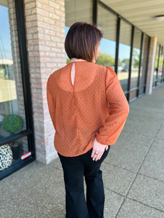 Woman wearing orange polka dot blouse with keyhole back detail, standing on covered walkway.