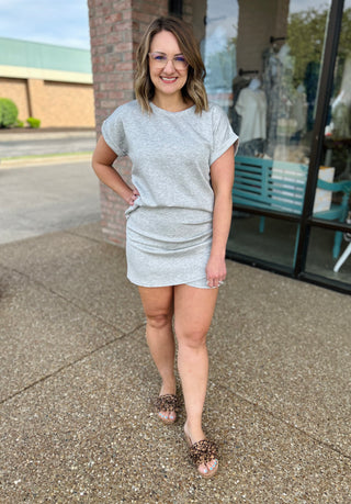 Woman wearing grey short-sleeve comfort top and matching skirt, standing outdoors in casual summer outfit.