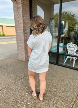 Woman wearing grey casual oversized t-shirt dress, shown from behind on outdoor patio.