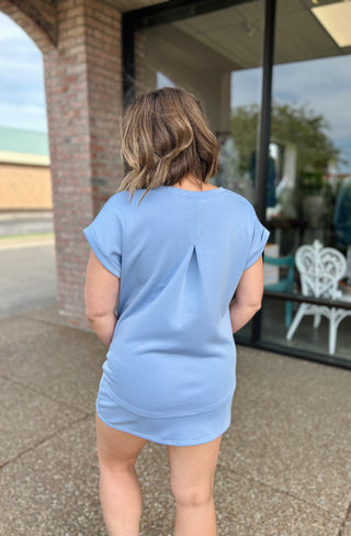 Woman wearing light blue short-sleeve comfort top, shown from behind in casual outdoor setting.