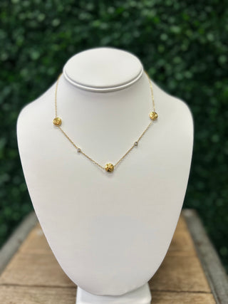 Gold chain necklace with textured disc charms displayed on white jewelry bust stand outdoors.